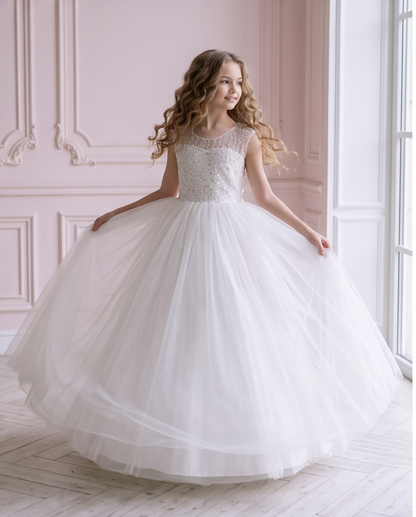 Girl holding out the full tulle skirt of the Celestial Grace white sequin communion dress beside a window.