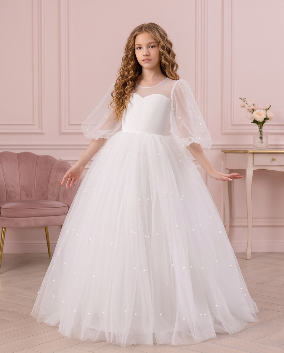 Girl wearing the Pearl Reverie white communion dress beside a floral fireplace, showing the full skirt.