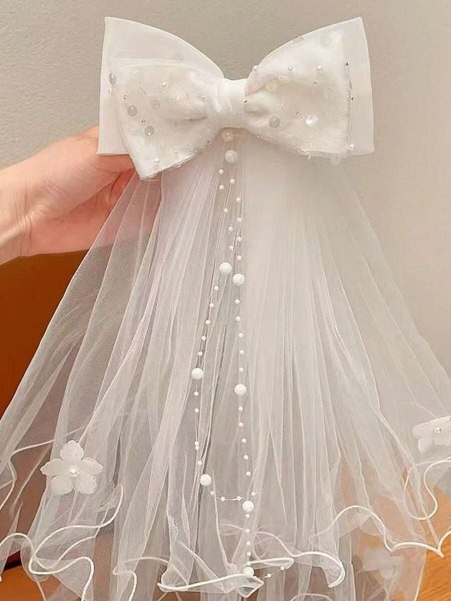 White pearl dot tulle bow communion veil with pearl chain trail and 3D flowers, held up against plain background