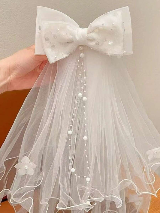 White pearl dot tulle bow communion veil with pearl chain trail and 3D flowers, held up against plain background