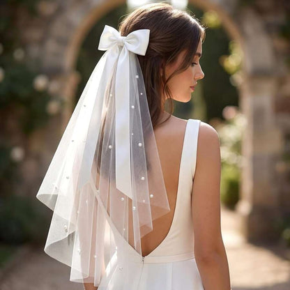 Girl wearing white pearl dot tulle veil with satin bow clip, back view in garden setting