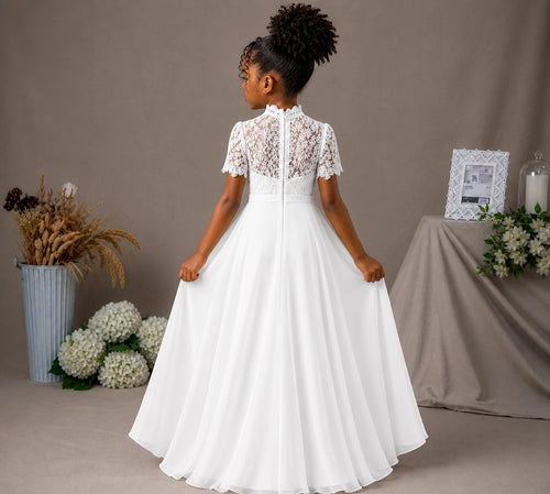 Young girl in a white dress standing in front of a neutral background with flowers and decor.