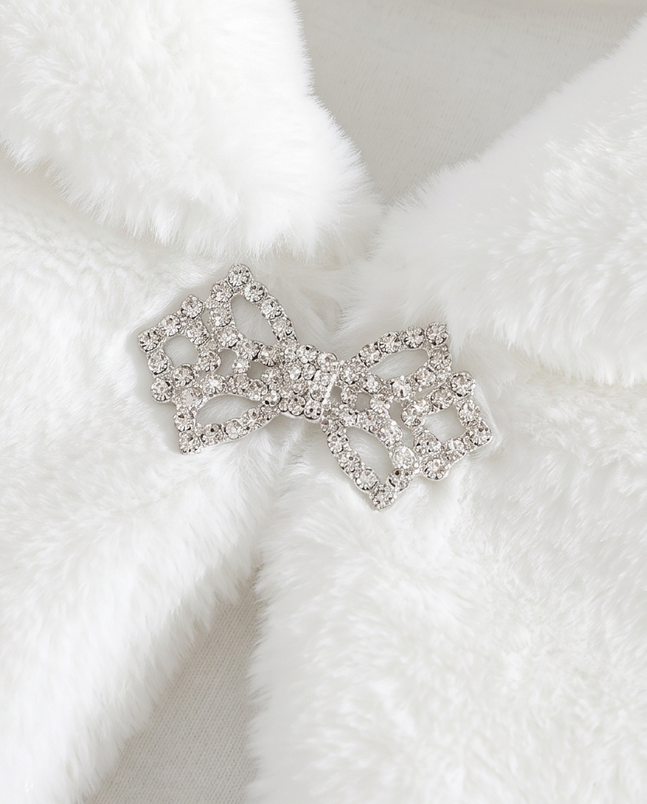 Silver bow-shaped brooch with clear gemstones on a white fur background