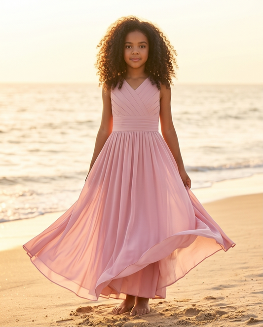 Young girl in a pink dress standing on a beach at sunset