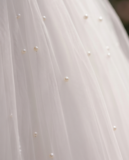 Close-up of a white tulle fabric with small pearls, likely from a wedding dress or bridal gown.