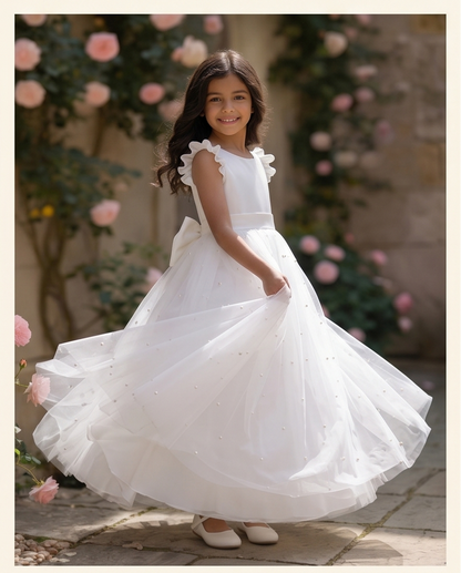 Young girl in a white dress standing outdoors with floral decorations.