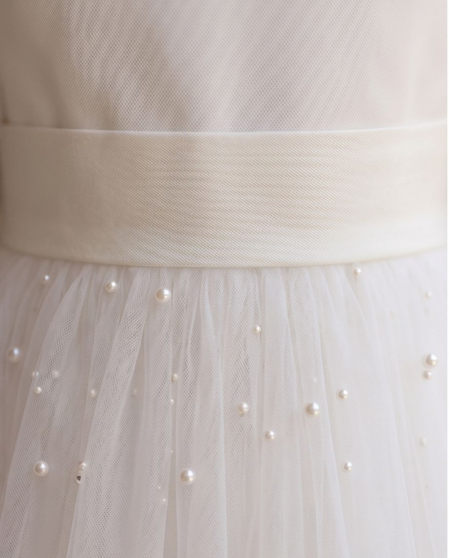 Close-up of a white dress with a belt and pearl embellishments.