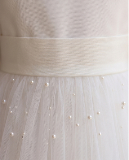 Close-up of a white dress with a belt and pearl embellishments.
