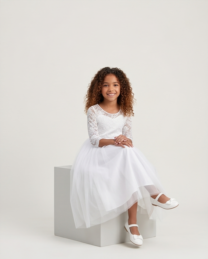 Young girl in a white dress sitting on a white box against a plain background