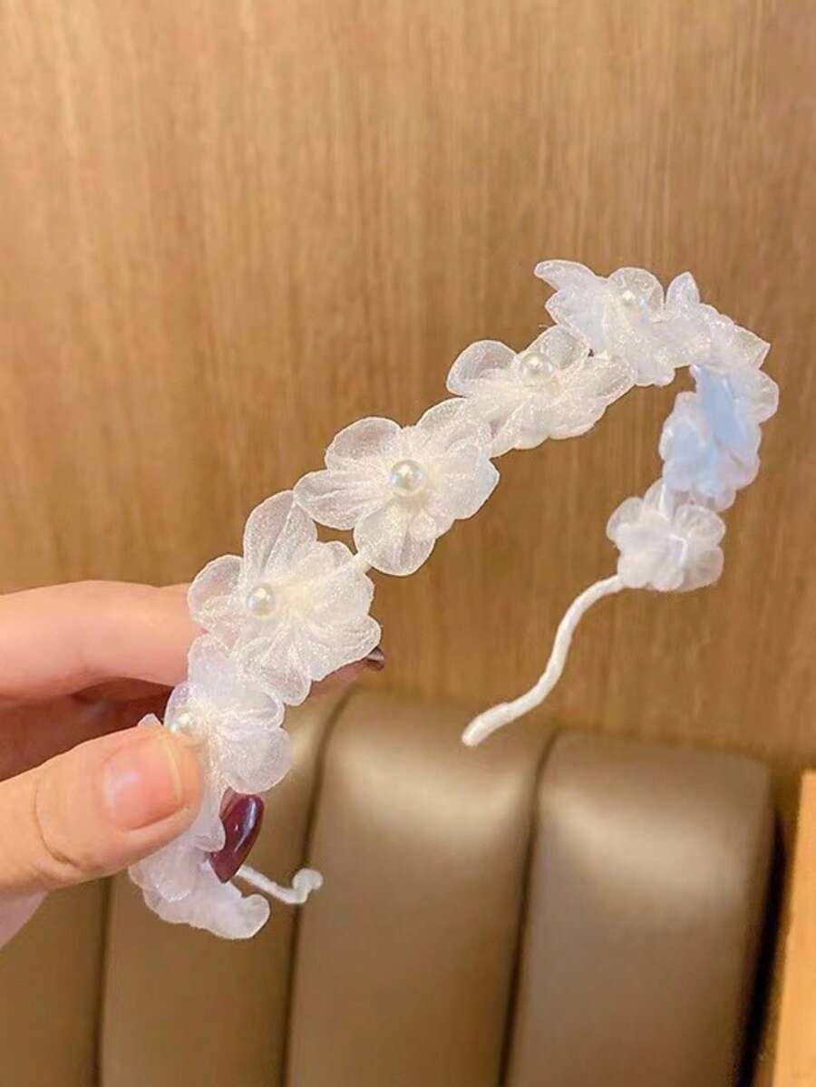 White floral headband held by a hand against a wooden background