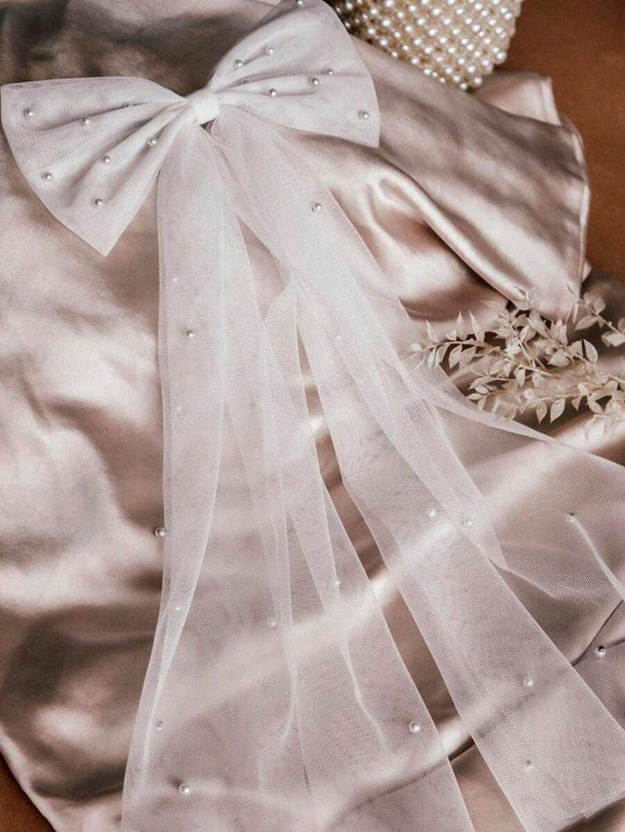 Light pink fabric with a large bow and pearl embellishments on a neutral background