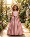Young girl in a pink dress standing in a garden with statues and plants.