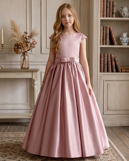 Young girl in a pink dress standing in a room with a fireplace and bookshelf.