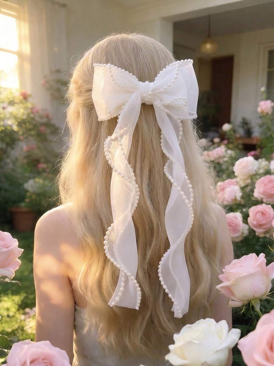 Person with long blonde hair wearing a large white bow in a garden setting