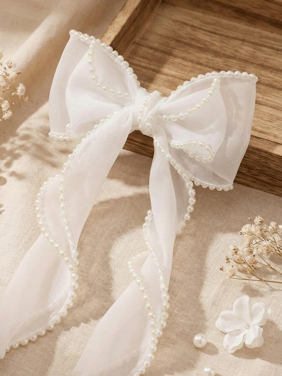 White bow with pearl details on a wooden surface with dried flowers.