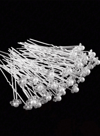 Large set of white pearl and rhinestone flower U-pins fanned out on black background showing quantity and detail