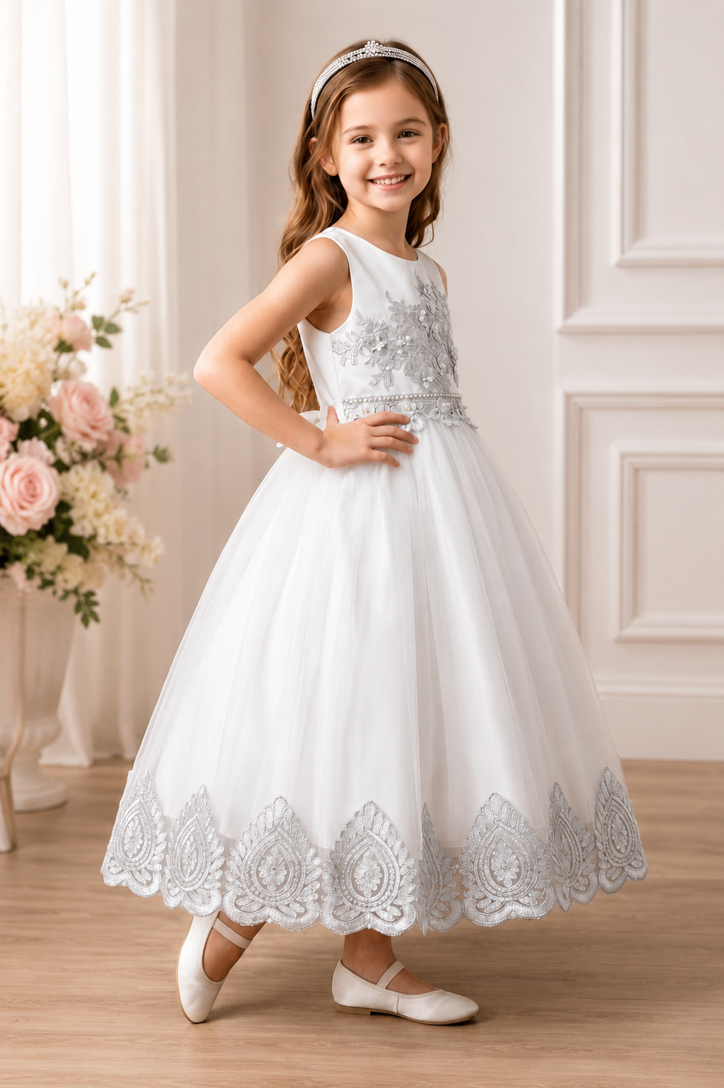 Young girl in a white lace dress standing in a room with floral decorations.