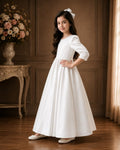 Young girl in a white dress standing in a room with wooden paneling and floral decorations.
