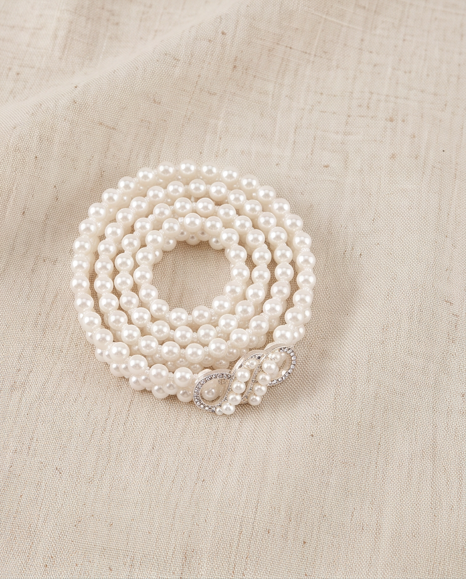 White pearl-look infinity clasp communion belt coiled on a neutral fabric background