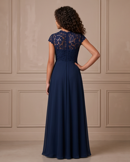 A woman wearing a navy blue floor-length formal dress, shown from the back. The dress features a lace cap sleeves and a sheer lace back panel, with a solid navy blue skirt.