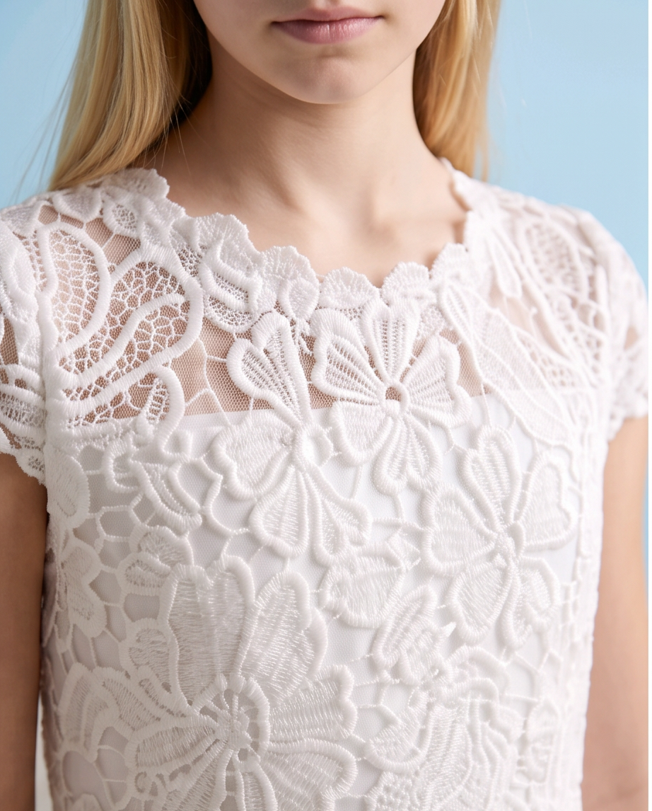 A close-up of a model wearing a white lace top with intricate floral embroidery and sheer mesh details, set against a light blue background.