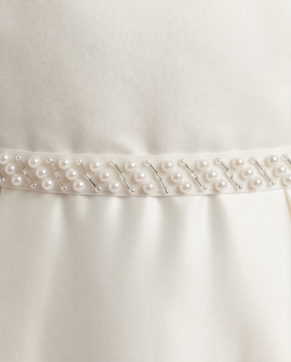Close-up of a white satin fabric with a row of pearls on a plain background
