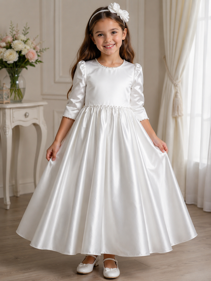 Young girl in a white dress standing in a room with a vase of flowers on a table.