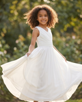 Young girl in a white dress standing outdoors with greenery in the background