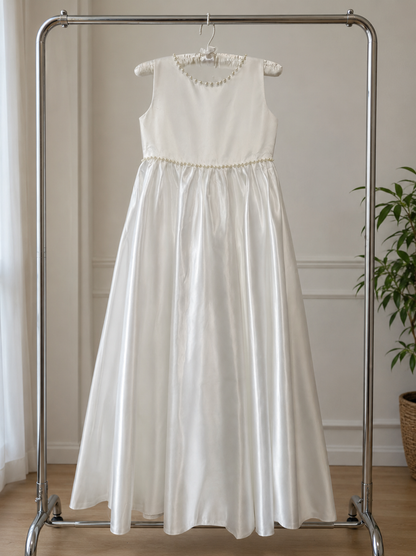 White dress with beaded neckline on a metal clothing rack against a neutral wall.