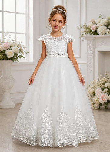 Young girl in a white lace dress standing in a decorated room with flowers.