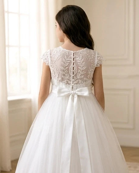 White lace dress with a bow on a person standing in a room with light-colored walls.